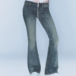 Lågmidjade Cheap Monday jeans  - Säljer ett par blå bootcut jeans från Cheap Monday med klassisk logga bak. Jeansen har låg midja, fem fickor och snyggt slitna detaljer framtill. Materialet är jeans i bomull och passformen är normal med utsvängda ben.