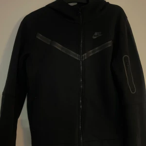 Svart Nike Tech Fleece hoodie - Svart Nike Teck Fleece i storlek XL (158-170). Sparsamt använd, ingen slitage, hål el liknande.