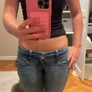 Lågmidjade blå jeans från OJAKO - Säljer ett par snygga lågmidjade jeans från OJAKO i klassisk blå tvätt. Jeansen är bootcut , coola detaljerade fickor med knappar bak och fram samt diskreta slitningar. 