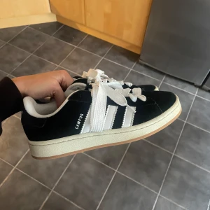 Svarta Adidas Campus sneakers  - Klassiska Adidas Campus sneakers i svart mocka med vita detaljer och breda vita snören. Använt en gång. 