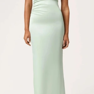 Ljusgrön långklänning med omlott - Säljer en elegant ljusgrön långklänning med omlottdetalj vid midjan. Klänningen har en figurnära passform och är ärmlös, vilket ger en stilren och modern look. 