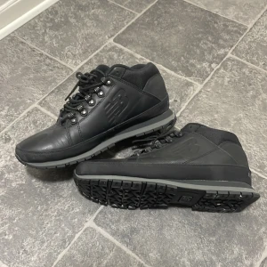 Vinter/höst skor från New Balance - Svarta kängor från New Balance med robust sula och snörning. Ovandelen är i skinn och textil, med metallöglor för snörningen och diskret logga på sidan. Perfekta för höst och vinter när du vill ha både stil och funktion.