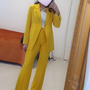 Gul kostym från Zara med kavaj och ett par byxor - Säljer en riktigt snygg gul kostym från Zara med rak kavaj och matchande vida kostymbyxor. Kavajen har klassisk krage, knappstängning och fickor fram. Byxorna har hög midja och pressveck. Perfekt för dig som vill sticka ut med färg!