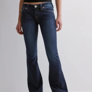 Mörkblå bootcut jeans från True Religion - Snygga mörkblå jeans från True Religion med bootcut passform och låg midja. Jeansen har klassiska kontrastsömmar, ficklock med knappar bak och ikoniska detaljer på bakfickorna. Perfekta för dig som gillar en retro vibe och markerad siluett.