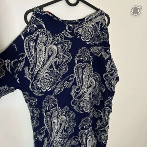 Mörkblå mönstrad klänning från Motel - Säljer en snygg mörkblå klänning från Motel med vitt paisleymönster. Klänningen har en asymmetrisk axel och är tillverkad i ett lätt material som känns skönt mot huden. Perfekt för dig som gillar unika detaljer och mönster.