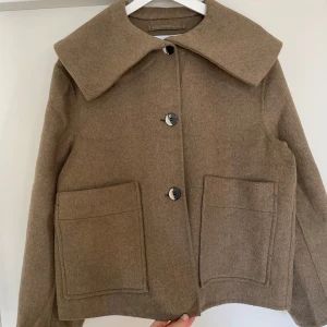 Beige ulljacka från Ganni - Säljer en beige ulljacka från Ganni med oversized krage och stora fickor framtill. Jackan har knäppning med tre knappar och en boxig, loose passform. Den är aldrig använd så jackan är i perfekt skick😊💕
