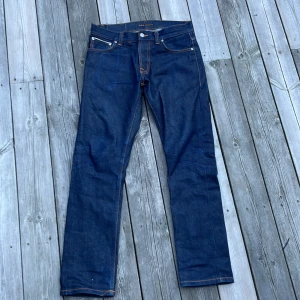 Nudie Jeans Grim Tim Dry Japan Selvage - Säljer ett par Nudie Jeans Grim Tim Dry Japan Selvage i mörkblå denim med klassiska orange sömmar och signaturbroderi på bakfickorna. Modellen har rak passform och är tillverkad i 98% bomull och 2% elastan för extra stretch. Riktigt snygga jeans med premiumkänsla. På sista bilden kan man se hur dessa kommer utvecklas och se ut vid längre användning. Tjecks inte på att höra av dig minsta fråga. Pris kan diskuteras vid snabb affär.