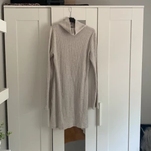 Beige ribbad stickad klänning Gina Tricot - Supermysig beige stickad klänning från Gina Tricot i ribbat material. Klänningen har långa vida armar,och en slits längst ner!