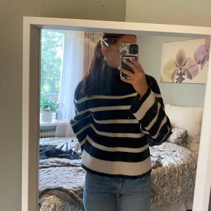 Randig svartvit stickad polotröja - Säljer en svart och vit randig stickad polotröja med breda ärmar och ribbad struktur. Tröjan har en loose passform och är perfekt för kyligare dagar. Snygg att styla med jeans eller kjol för en avslappnad look.