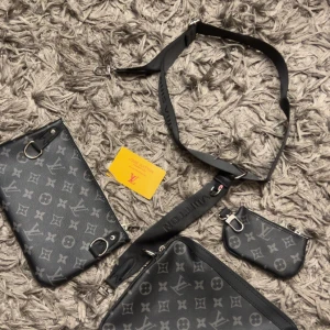 svart axelväska monogram - Säljer en svart axelväska med klassiskt monogrammönster. Väskan har flera fack och en justerbar axelrem med-tryck. Tillverkad i skinn med silverfärgade detaljer och dragkedjor. Perfekt för dig som vill ha en stilren och lyxig accessoar.