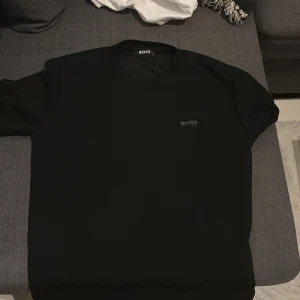 Svart t-shirt från Hugo Boss - Snygg svart t-shirt från Hugo Boss med diskret logga på bröstet. Klassisk rund halsringning och korta ärmar. Perfekt basic-plagg med stilren design och skön passform. Materialet känns mjukt och följsamt.