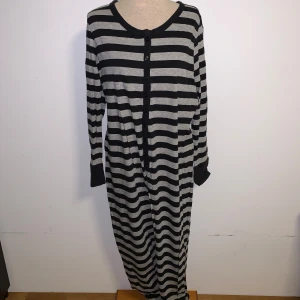 Randig jumpsuit från Jolinesse - Säljer en jättemysig pjsmas från Jolinesse med svarta och gråa ränder. Jumpsuiten har långa ärmar, rund hals och knappar framtill. 