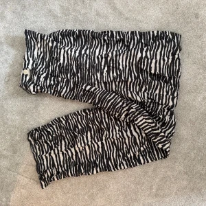 Zebramönstrade vida byxor - Säljer ett par riktigt snygga byxor med svartvitt zebramönster. De har en lös och wide passform med hög midja och knappstängning framtill. Perfekta för dig som vill sticka ut lite extra och gillar djurmönster.