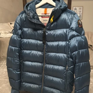 Parajumper pharrell jacket - Säljer en blå dunjacka från Parajumpers. Jackan har en glansig finish, huva, dragkedja framtill och cool gul detalj vid halsen. Klassisk Parajumpers-patch på ärmen och två fickor med dragkedja. Perfekt för hösten och vintern. Nypris är ca 6000kr. Köpt på Thernlunds. Väldigt fint skick. 