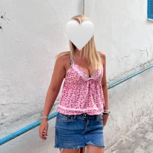 Rosa blommig linnetopp  - Supersöt rosa linnetopp med blommigt mönster och tunna axelband. Toppen har v-ringning och fina spetsdetaljer längs kanten. Perfekt för varma dagar och ger en riktigt somrig vibe.