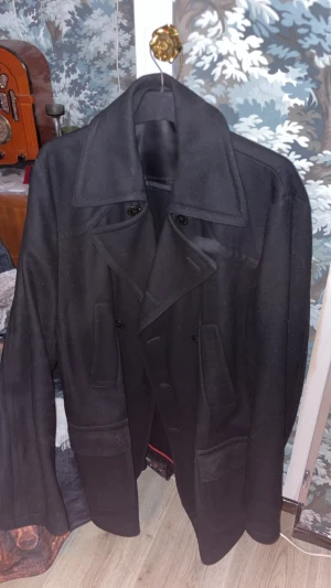 Svart skepparkavaj från Hugo - Säljer en svart skepparkavaj från Hugo boss, storlek L, nypris 3664 kr klassisk dubbelknäppning och bred krage. Jackan har stora fickor framtill och snygga röda detaljer på insidan. Materialet är ullblandning som ger en schysst och stilren look. Perfekt för dig som vill ha en tidlös jacka med edge. Använd fåtal gånger 