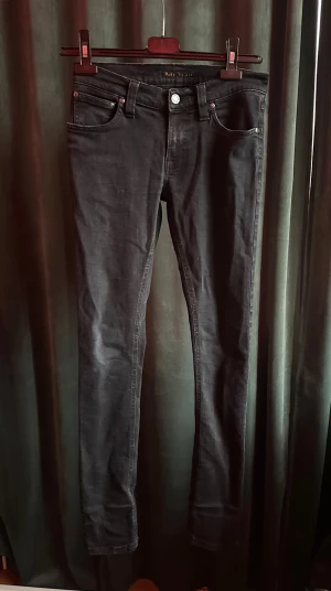 Svarta skinny jeans från Nudie Jeans - Snygga svarta jeans från Nudie Jeans med klassisk femficksdesign och silverfärgad knapp. Modellen är skinny med smal passform och raka ben. Jeansen har hög midja och är tillverkade i mjukt jeanstyg med stretch för extra komfort.  Str W 26 L. Pris 299kr men kan diskuteras såklart.