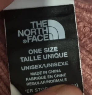 Rosa stickad mössa från The North Face - Snygg rosa mössa från The North Face med ribbad stickning och uppvikt kant. Stor svart och vit logotyp framtill ger en clean och modern look. Perfekt för kalla dagar och passar både tjejer och killar.