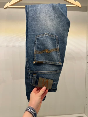 Nudie Jeans blå slim Jeans W24 L28  - Snygga blå jeans från Nudie Jeans i modellen skinny med klassisk orange söm på bakfickan. Jeansen har normal passform, fem fickor och är tillverkade i mjukt jeanstyg. Perfekt för dig som gillar en smal siluett och stilren look. Jag är 167 och sitter förstort