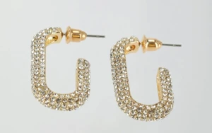 Glittriga guldörhängen med stenar - Säljer ett par chunky örhängen i guld med massor av glittrande stenar. De har en fyrkantig, böjd form och är perfekta för att ge din look extra bling. Örhängena har stift och är riktigt statement med sin glittriga yta.