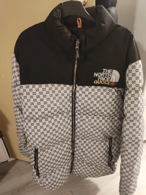 Gucci x The North Face pufferjacka XL - Exklusiv pufferjacka i samarbete mellan Gucci och The North Face. Jackan är svart upptill och vit nedtill med all-over GG-mönster, broderad logga på bröstet och dragkedja framtill. Fodret är orange och jackan har två fickor med dragkedja.