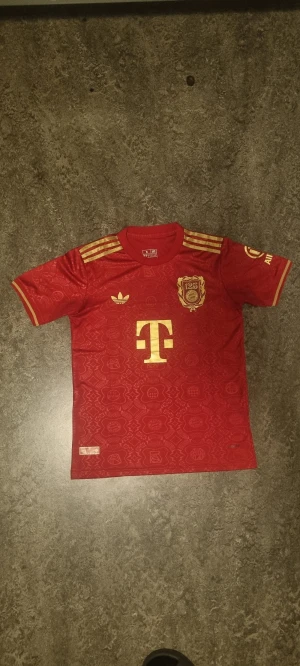 Röd Bayern Munich Speciall Tröja - Röd och Guld Bayern Munich apeciall tröja. Skön mjuk material, slim fit på armarna och formen tröjan passar mig perfekt som är (175cm 70kg) men den skulle även passa ngn lite mindre elr större.
