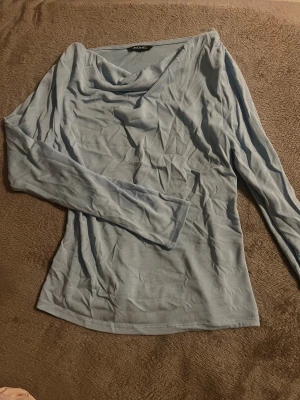 Ljusblå långärmad topp från Monki - Säljer en ljusblå långärmad topp från Monki med snygg draperad halsringning. Tunn och mjuk i materialet, perfekt för dig som gillar stilrena och enkla plagg. 