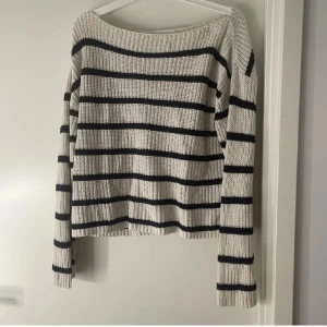 Randig stickad tröja vit och svart - Snygg stickad tröja med breda svarta ränder på beige botten. Tröjan har en avslappnad passform, ribbade muddar och lång ärm. Perfekt för lager-på-lager och passar till både jeans och kjol.