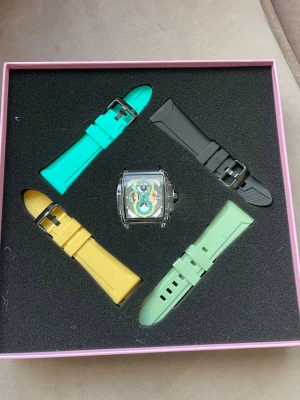 F5 fyrkantig kronografklocka med färgband - Cool fyrkantig kronografklocka från F5 med transparent boett i silverfärgat rostfritt stål. Urtavlan har detaljer i turkos, gult och svart. Medföljer fyra utbytbara silikonband i svart, turkos, gul och ljusgrön. Perfekt för dig som gillar att variera din stil.