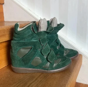 Gröna Isabel Marant sneakers med klack - Säljer ett par gröna Isabel Marant skor med inbyggd klack och cool design. Skorna har mocka och skinnpaneler, kardborreband och rund tå. Yttersulan är gummimönstrad och märkt med Isabel Marant. Perfekt för dig som vill ha en mindre basic outfit. Pris går att diskutera vid snabbt köp 