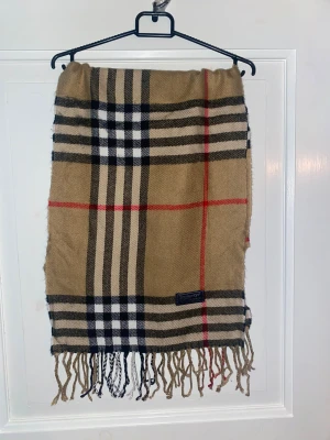 Beige Halsduk från Burberry - Beige halsduk från Burberry i 100% merinoull. Väldigt fint skick till ett bra pris. Mitt pris: 399kr