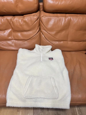 Vit fleece half zip från GANT - Supermjuk och fluffig vit fleece-tröja från GANT med broderad logga på bröstet. Tröjan har en praktisk half zip, hög krage och stor magficka. Perfekt för kyliga dagar när du vill vara både varm och snygg.