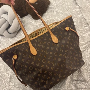 Väska  - Säljer en klassisk Louis Vuitton i brunt med ikoniskt monogrammönster och ljusbruna skinnhandtag. Insidan är beige med svarta ränder och logotyptryck. Väskan har rymligt fack och snygga detaljer i skinn.