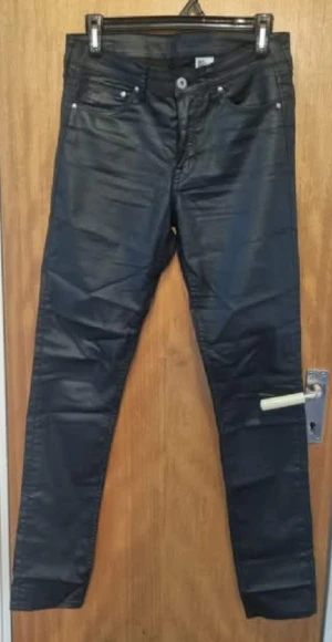 Svarta skinny jeans med glansig finish - Snygga svarta jeans med glansig finish och skinny passform. Klassisk femficksmodell med knapp och dragkedja framtill. Perfekta för dig som gillar en stilren look med lite edge.