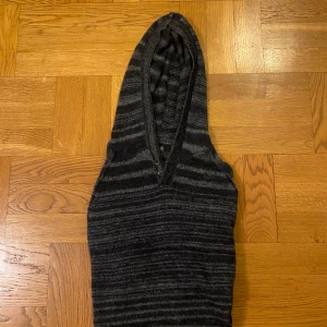 Randig mörkgrå hoodie med knappar - Mysig hoodie från Kenneth Cole i mörkgrått och ljusgrått randigt mönster. Tröjan har huva, två knappar vid halsen och är långärmad. Stickad i mjukt material. Snygg och enkel att matcha med jeans👍