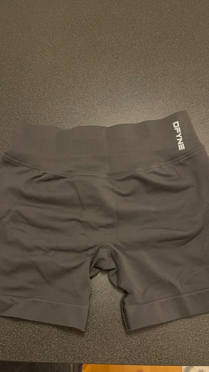 Gråa seamless träningsshorts DFYNE - Säljer ett par grås seamless träningsshorts från DFYNE i storlek S. De har hög midja, ribbad linning och scrunch-detalj bak för extra form. Materialet är stretchigt och består av 90% polyamid och 10% elastan, perfekta för gymmet eller löpning.