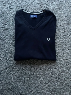 Fred Perry tröja - V-ringad tröja i marinblå färg. Det är en tunn bomullströja i bra skick! Hör av er om ni har frågor!