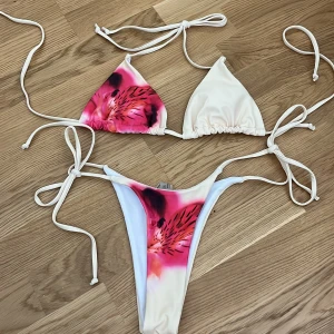 Blommig bikini med knytband - Superfin bikini med blommigt mönster i rosa, rött. Triangeltopp med knyt i nacke och rygg samt matchande trosa med knyt i sidorna. Perfekt för stranden och sommarens alla bad.