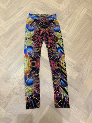 Färgglada leggings med grafiskt mönster - Säljer ett par riktigt coola leggings med ett galet grafiskt mönster i blått, rött, gult, orange och svart. De har en tajt passform och är gjorda i stretchigt syntetmaterial. Perfekta för dig som vill sticka ut och gillar färgexplosioner!
