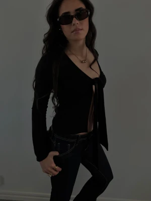 Snygg knyttopp  - Säljer en svart knyttopp med långa ärmar och djup v-ringning. Toppen har en snygg knytning framtill som ger en öppen look. Perfekt att styla med jeans eller kjol!