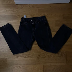 Levi's 501 svarta jeans W25 L30 - Svarta Levi's 501 jeans med klassisk rak passform och femficksdesign. Jeansen har knappgylf och är tillverkade i robust denim av bomull. Perfekta för dig som gillar en tidlös och clean look. Storlek W25 L30.