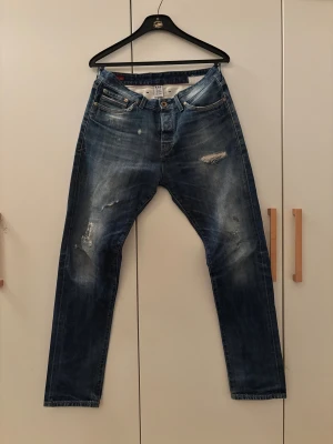Blå jeans Jack & Jones R.D.D. W33/L32 - Säljer ett par blå jeans från Jack & Jones Royal Denim Division. Jeansen har slitna detaljer och en tvättad look, klassisk femficksmodell och raka ben. Materialet är jeans i bomull och passformen är normal. Perfekta för dig som gillar en avslappnad stil.