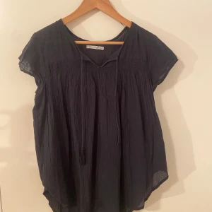 Svart blus från Black Story med snörning - Svart blus från Black Story i luftig bomull med korta ärmar och snörning. Ena snöret har tappat sin toffs men de är inget som stört mig när jag burit den🥰