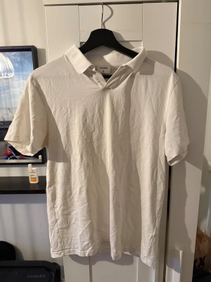 Vit pikétröja från Filippa K - Klassisk vit pikétröja från Filippa K i mjuk bomull. Tröjan har korta ärmar, krage och en stilren design utan synliga knappar. Perfekt för en clean och enkel look. Passar dig som gillar minimalistisk stil.