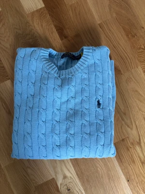 Ljusblå stickad tröja Polo Ralph Lauren - Snygg ljusblå kabelstickad tröja från Polo Ralph Lauren i storlek M. Tröjan är i bra skick och knappt använd. Hör av dig vid några frågor eller funderingar 