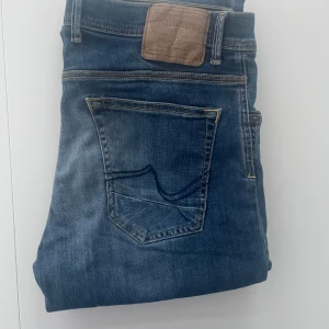 Blå jeans från Petrol Industries W33 L32 - Säljer ett par klassiska blå jeans från Petrol Industries i regular fit. Jeansen har raka ben, snygga slitningar och detaljerade bakfickor med kontrastsömmar. Perfekt passform och stilren look för dig som gillar en avslappnad vibe.