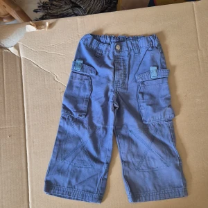 Blå cargopants från Friends, stl 86 till barn - Säljer ett par blå cargopants från Friends i storlek 86. Byxorna har resår i midjan, stora sidofickor med lock och coola sömdetaljer på benen. Tillverkade i 100% bomull för en skön känsla. Perfekta för lek och äventyr!