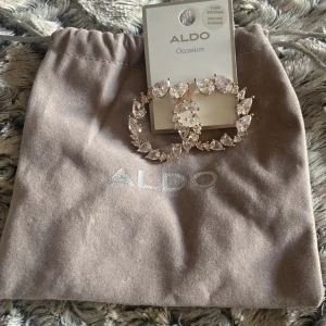 Glittriga örhängen från ALDO - Stora, runda örhängen från ALDO med gnistrande stenar i droppformad cubic zirconia. Örhängena har guldfärgad infattning och ger en riktigt lyxig känsla. Perfekta för dig som vill sticka ut och glänsa extra mycket.