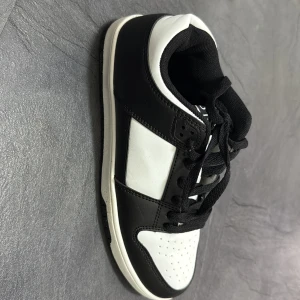 Svarta och vita sneakers i skinn - Snygga svartvita sneakers med klassisk design och kontrasterande paneler. Skorna har snörning, rund tå och platt sula. Ovandelen är i skinn och textil, med svart foder och vita detaljer. Perfekta för dig som gillar streetstyle och enkel, stilren look.