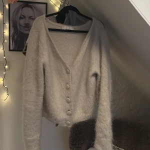 Beige fluffig kofta med knappar - Supermjuk och fluffig beige kofta från H&M med v-ringning och stora matchande knappar framtill. Långärmad och croppad modell som är perfekt för lager-på-lager. Enkel att styla till olika outfits och riktigt cozy känsla. Orginal pris 700kr